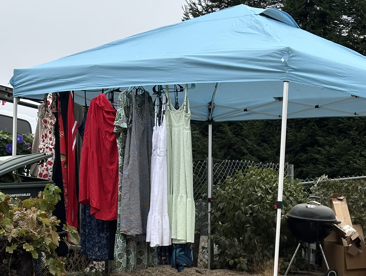 Dresses on a rack under a blue pop-up canopy, set up on a gravel lot.