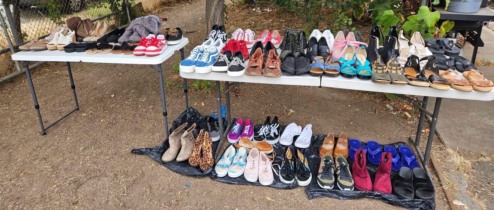 Two folding tables and a row on the ground holding more than forty pairs of shoes, grouped by kind and size.