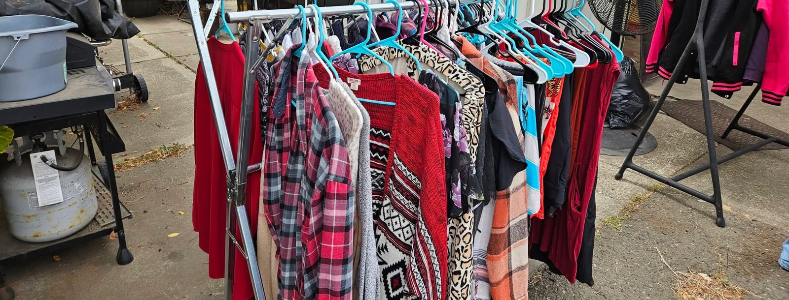 A rack of sweaters, flannel shirts and jackets standing beside the house, every piece on a teal hanger.